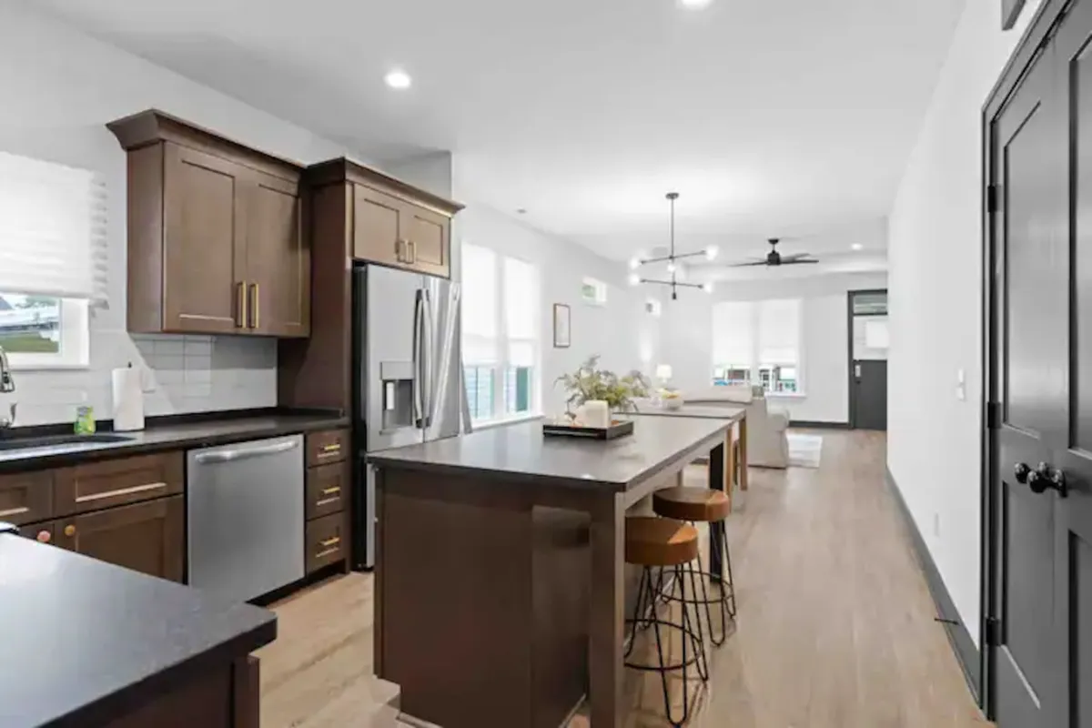 A welcoming kitchen highlighted by a large island with bar stools, stainless steel appliances, and an abundance of natural light pouring in from adjacent windows. The setup is ideal for entertaining, family gatherings, or dividing tasks between multiple cooks.