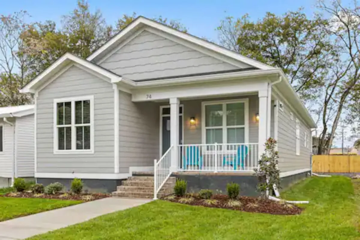 A cheerful exterior view featuring a front porch lined with colorful rocking chairs and a landscaped garden, capturing an inviting, social atmosphere. The porch setting suggests a space for gatherings and relaxing after a day exploring downtown.
