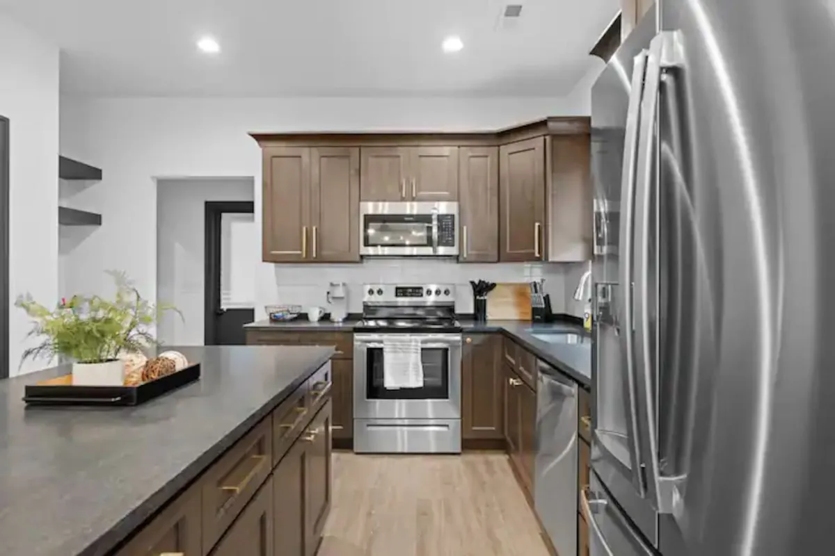A modern kitchen featuring a central island, stainless steel appliances, and wood cabinetry. The space is designed for socializing, with an open layout suitable for both casual meals and special gatherings.