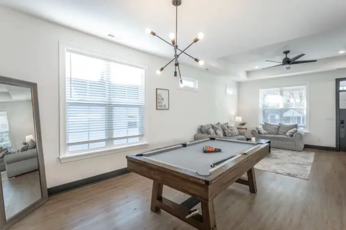 A relaxed game room setting with a pool table as the focal point, complemented by a cozy sofa and bright lighting. A stylish mirror and tasteful lighting add to the room's inviting ambiance, emphasizing the fun, social atmosphere.