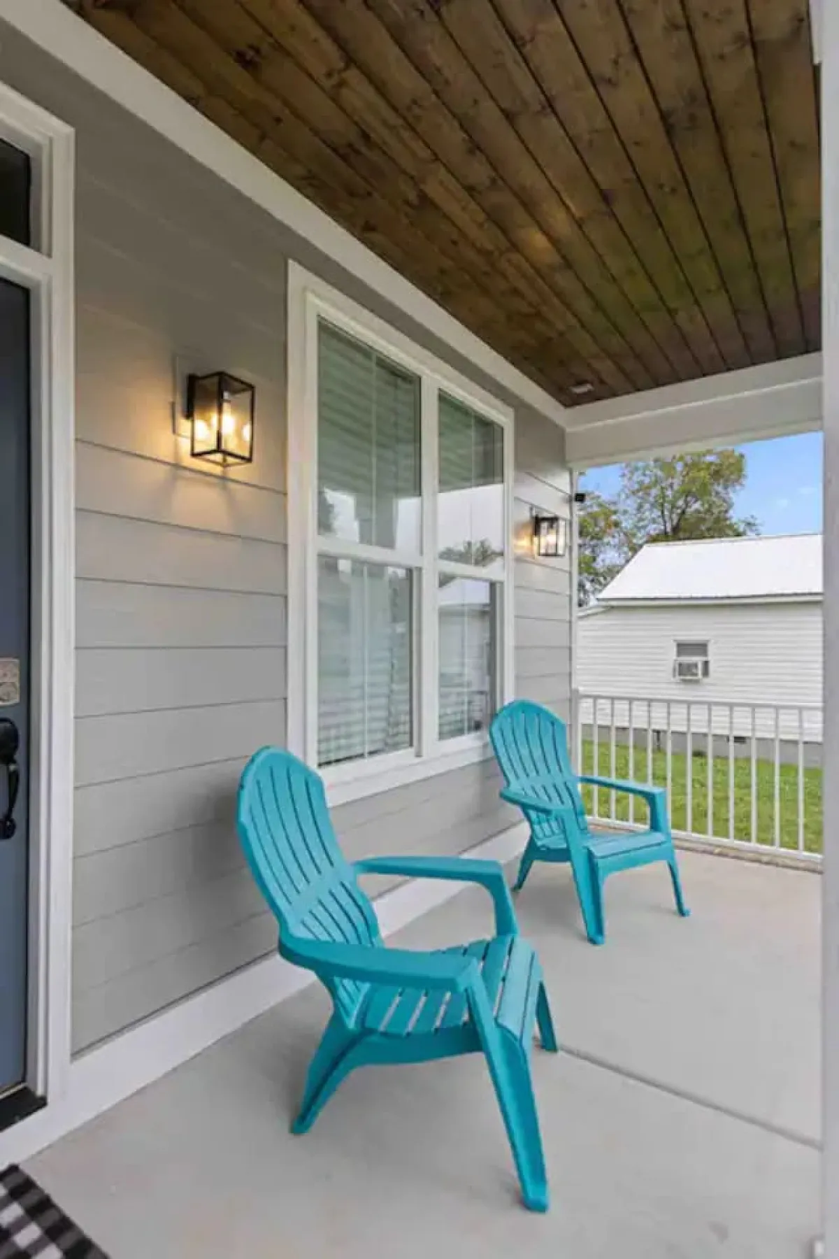 An inviting exterior view with turquoise Adirondack chairs and decorative light fixtures on a wooden-ceiling porch, suggesting a serene spot for outdoor socializing and evening celebrations.
