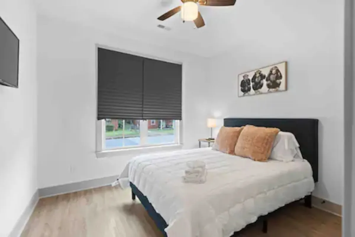 This cozy bedroom features a bed with plush pillows and a playful wall art piece of three monkeys. Natural light streams in from the window, creating a warm and welcoming environment. The space looks inviting, perfect for restful sleep and quiet moments in the morning.