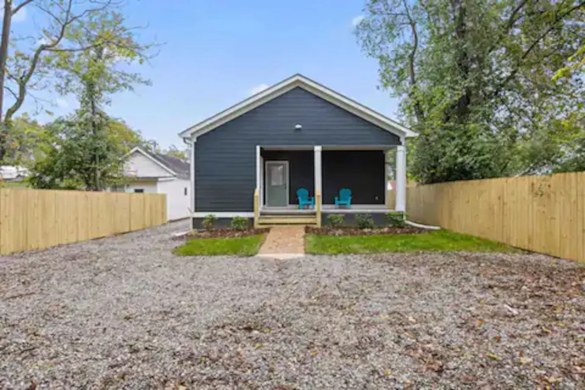 An exterior shot of a front porch with bright blue chairs and a lush, landscaped yard, evoking an atmosphere of relaxation and connection to nature. The view hints at easy access to outdoor activities and gatherings.