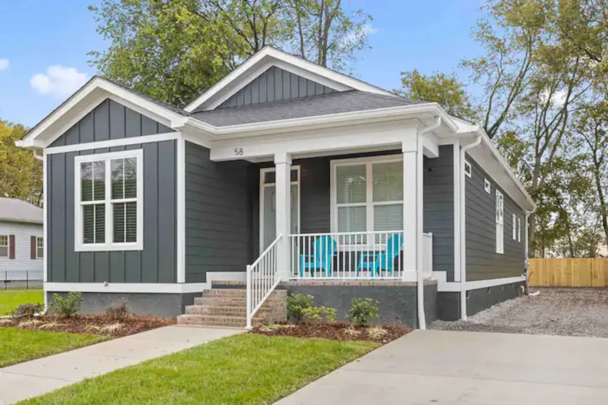 This image captures the exterior of a modern home with blue chairs on a welcoming porch and a well-maintained lawn, exuding an inviting and cheerful vibe. The setup hints at social gatherings and relaxation opportunities outdoors.